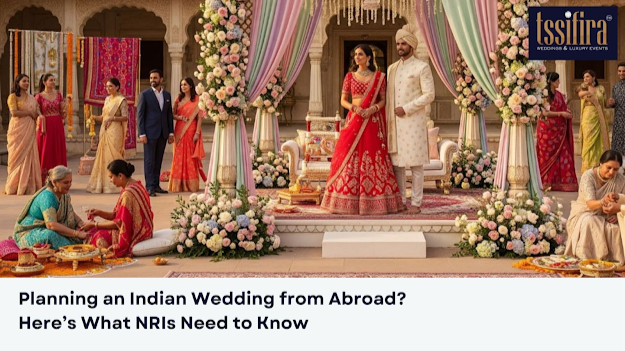 A luxurious Indian wedding ceremony with a bride in a red lehenga and groom in a cream sherwani standing on a beautifully decorated stage with pastel drapes and floral arrangements. Guests in traditional attire are engaged in rituals and conversations. The Tssifira Weddings logo is visible, with the text โPlanning an Indian Wedding from Abroad? Hereโs What NRIs Need to Know.โ